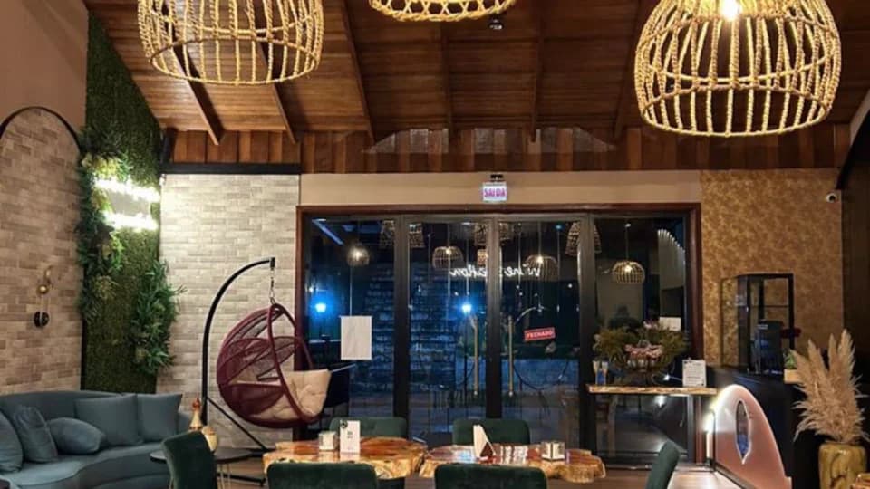 Mesas e cadeiras verdes sob luminárias de palha no restaurante Adegga