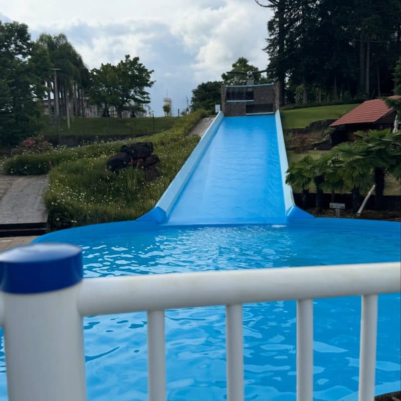 Rampa molhada azul descendo até a piscina, entre árvores