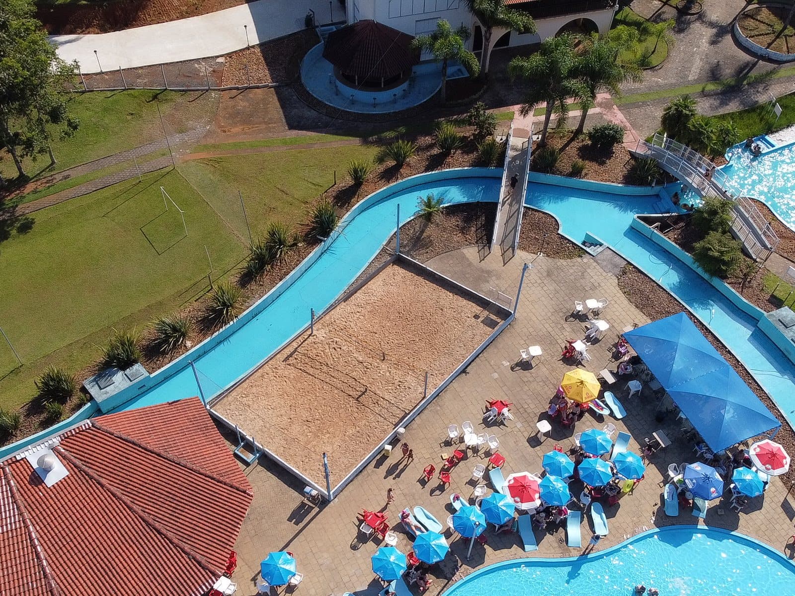 Quadra de areia vista do alto, ao lado do quiosque de telhado vermelho e das piscinas